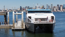 Photo of water taxi at Seacrest Dock in West Seattle on a sunny day, the Seattle skyline in the background.