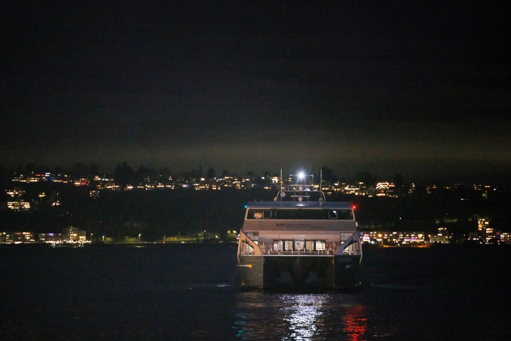 The Water Taxi glides at night through water reflecting city lights.